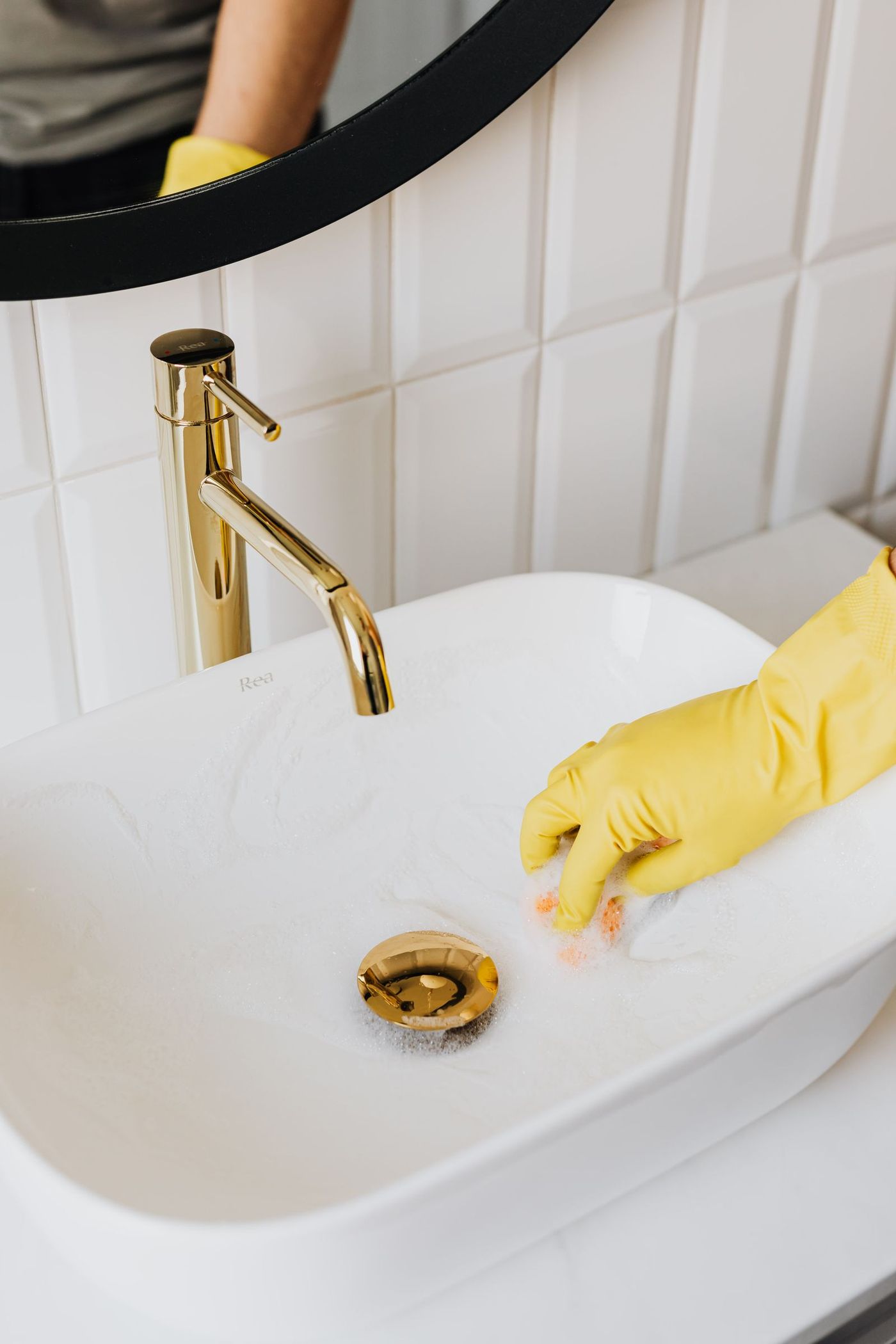 A gloved hand wiping a white bathroom sink until it shines