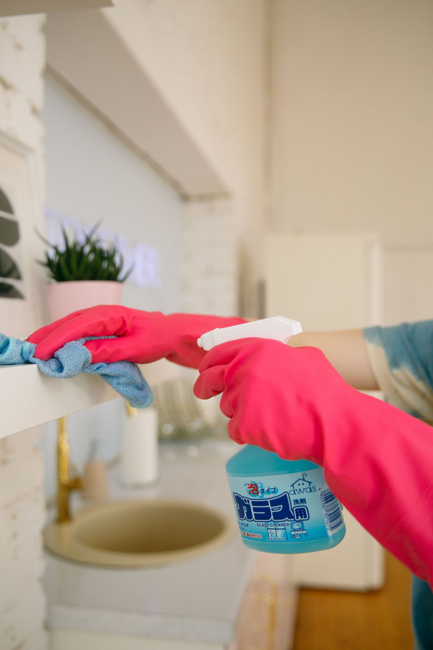 Pink-gloved hands spraying and wiping a bathroom counter